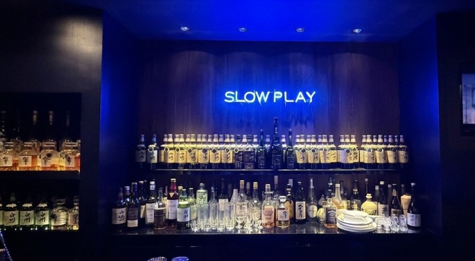 SLOW PLAYのネオンサインと酒類が並ぶバーカウンター